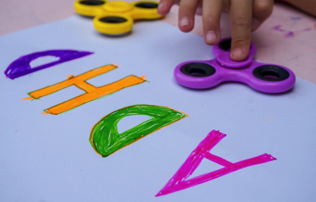 A close up of a finger on a fidget spinner and a paper with the word "ADHD." A play therapist in Atlanta, GA can offer support for your child's concerns. Learn more by searching "play therapy near me" today.