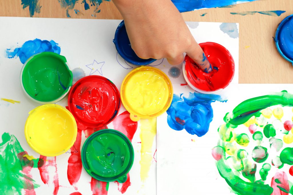 A top down view of a child dipping their finger into paint, representing play therapy in Atlanta, GA. Learn more about play therapy for kids in Atlanta, GA and other services by contacting a play therapist in Atlanta, GA today.